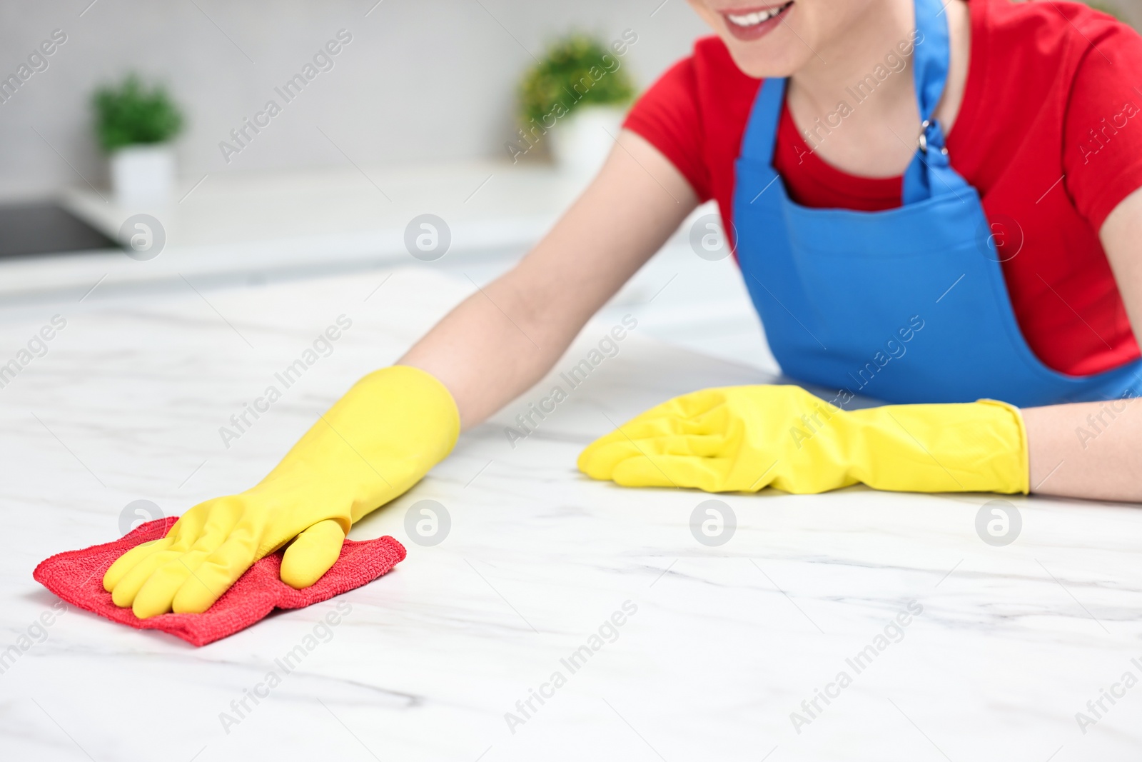 Photo of Woman cleaning white marble table with rag in kitchen, closeup