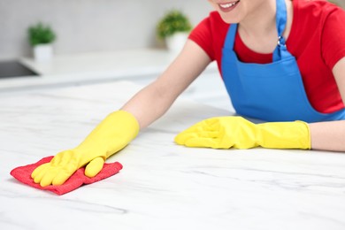 Photo of Woman cleaning white marble table with rag in kitchen, closeup