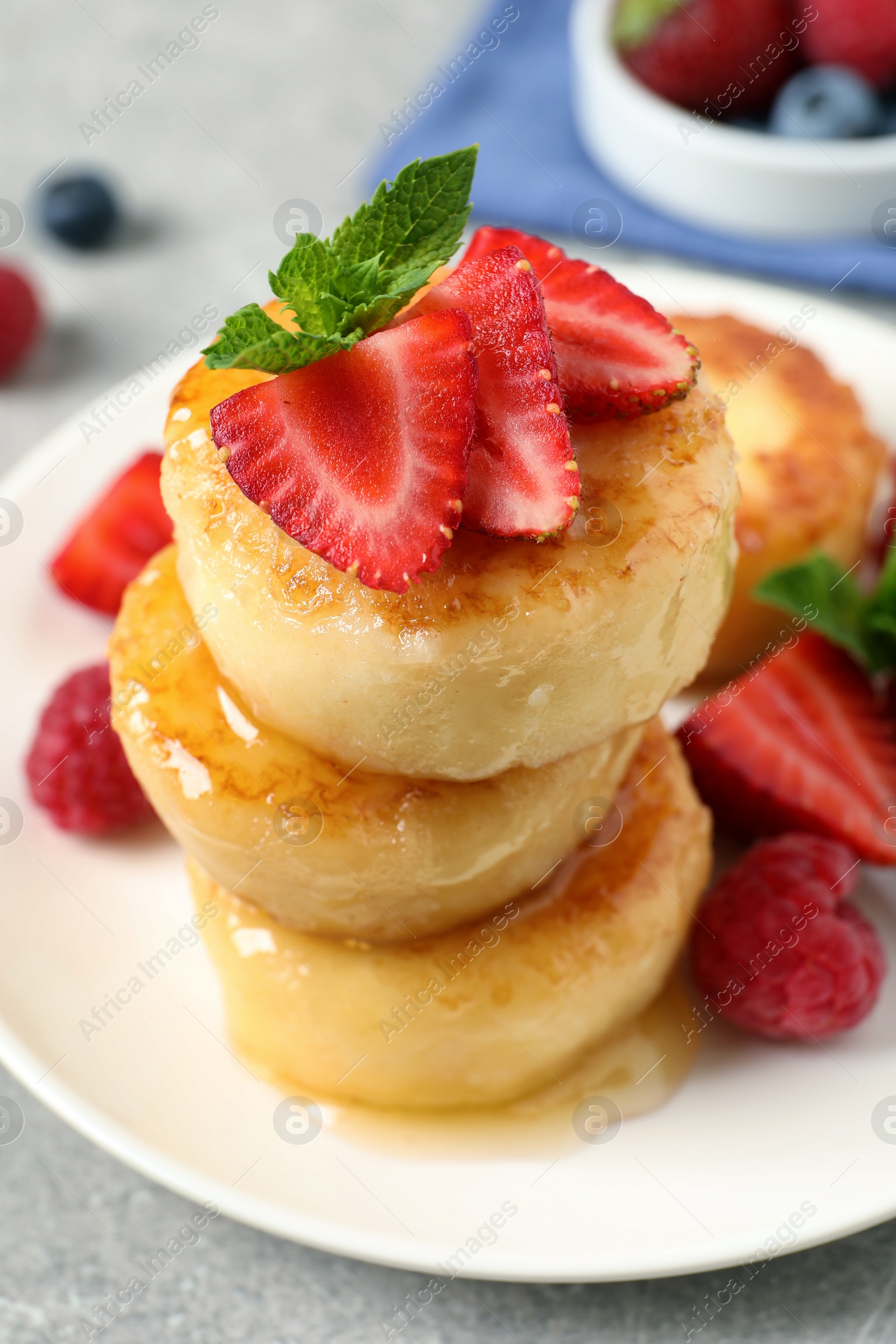 Photo of Delicious cottage cheese pancakes with fresh berries, mint and honey on light table, closeup