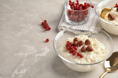 Photo of Creamy rice pudding with red currant and hazelnuts in bowls served on grey table. Space for text