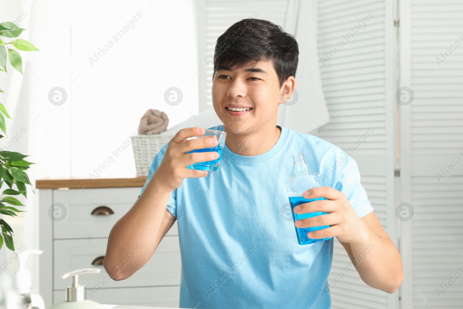 Photo of Man holding bottle and glass with mouthwash in bathroom. Teeth care