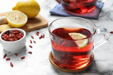 Photo of Healthy goji tea with lemon in glass cup on marble table