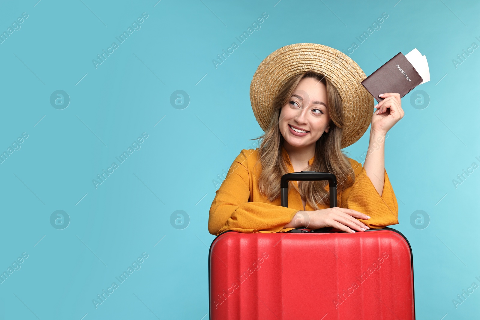 Photo of Happy young woman with passport, ticket and suitcase on light blue background, space for text
