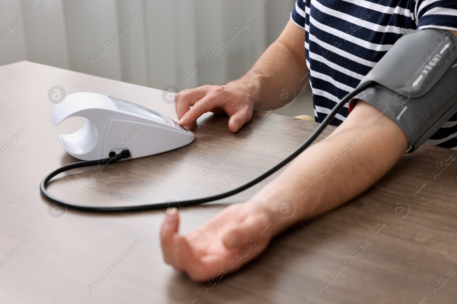 Photo of Man measuring blood pressure at wooden table, closeup