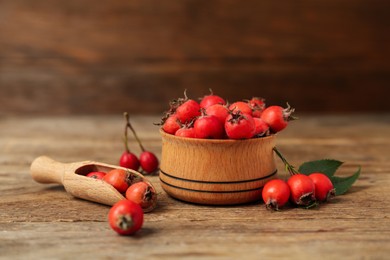 Photo of Ripe rose hip berries with green leaves and scoop on wooden table