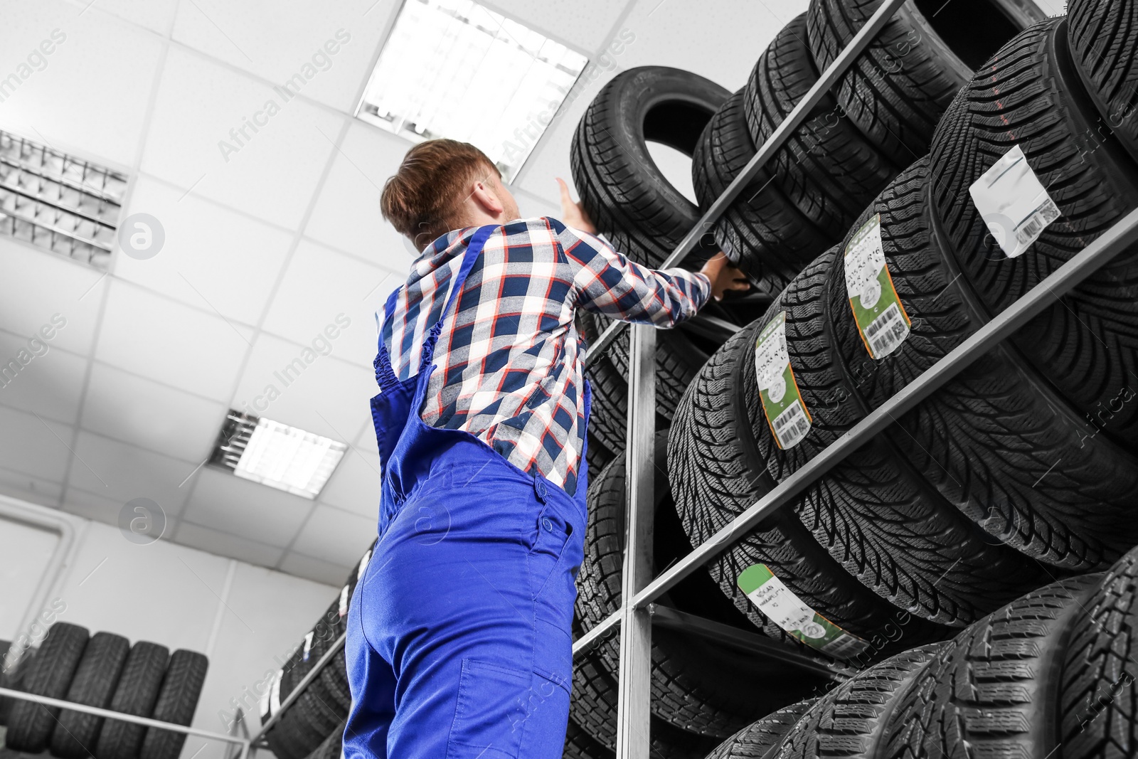 Photo of Young male mechanic with car tires in automobile service center