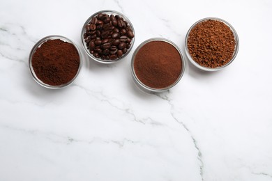 Bowls of beans, instant and ground coffee on white marble table, flat lay. Space for text