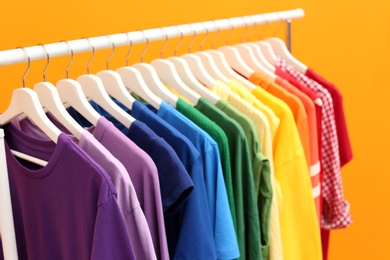 Photo of Rack with rainbow clothes on color background