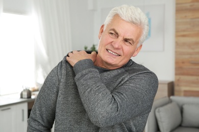 Photo of Mature man scratching shoulder at home. Annoying itch