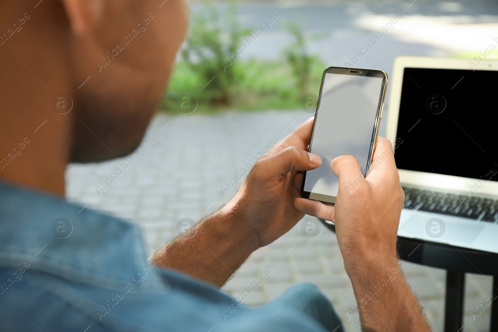 Photo of Man with smartphone and laptop in outdoor cafe, closeup