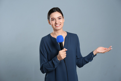 Young female journalist with microphone on grey background