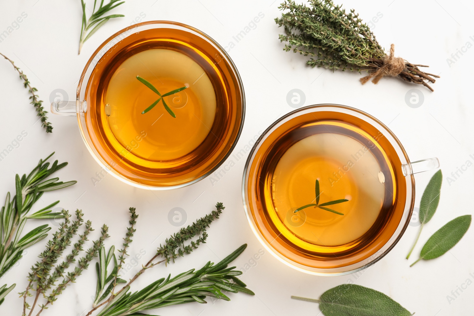 Photo of Cups of aromatic herbal tea with thyme, rosemary and sage on white marble table, flat lay