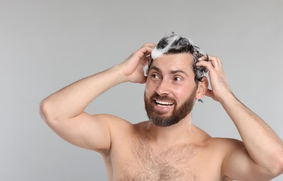 Happy man washing his hair with shampoo on grey background