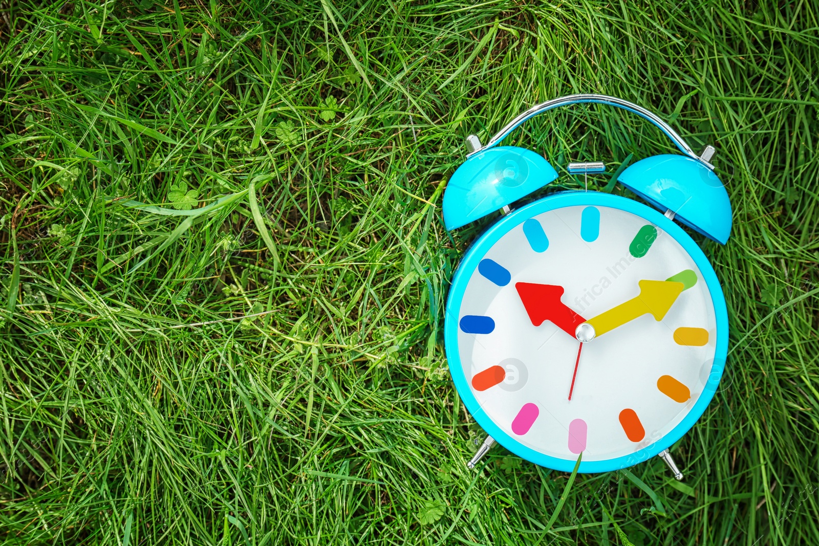 Photo of Alarm clock on green grass, outdoors. Time change concept