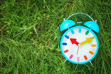 Alarm clock on green grass, outdoors. Time change concept