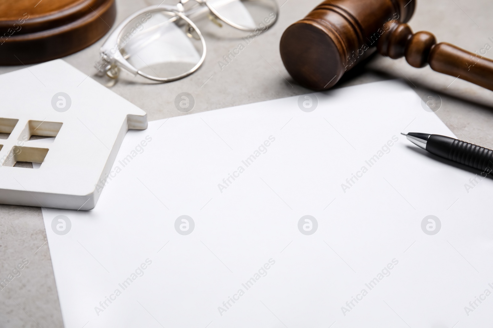 Photo of Last will and testament near house figure, glasses and gavel on light grey table, closeup