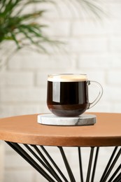 Photo of Glass mug of coffee with stylish stone cup coaster on wooden table in room
