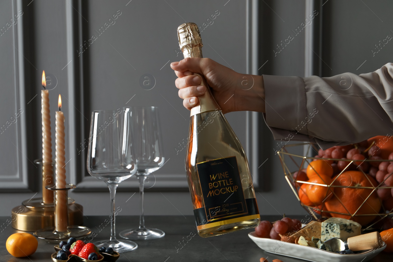 Photo of Woman holding bottle of sparkling wine over table with different snacks, closeup