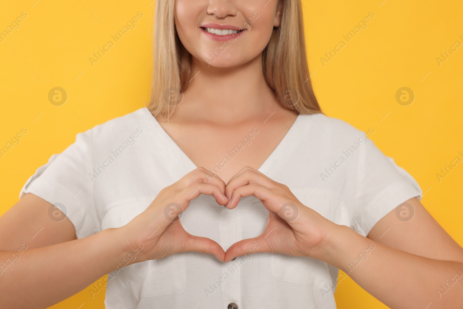 Photo of Happy volunteer making heart with her hands on orange background, closeup