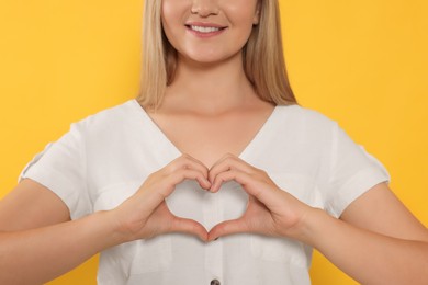 Photo of Happy volunteer making heart with her hands on orange background, closeup
