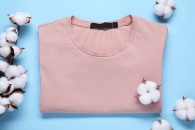 Cotton branch with fluffy flowers and beige t-shirt on light blue background, flat lay