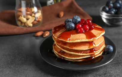 Stack of tasty pancakes with berries and syrup on table