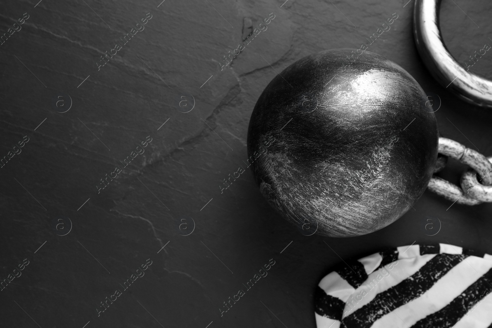 Photo of Prisoner ball with chain and jail cap on black table, flat lay. Space for text