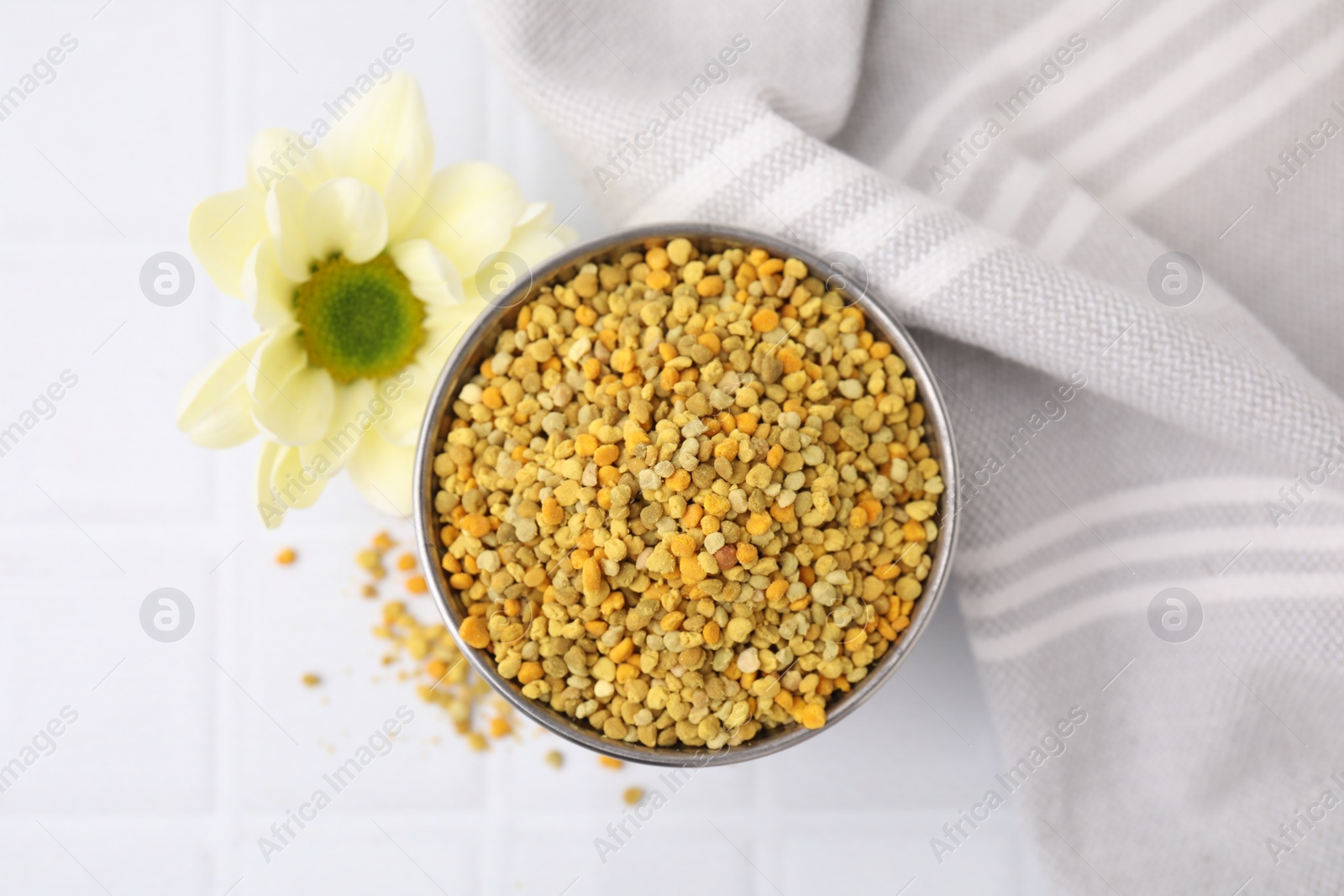 Photo of Fresh bee pollen granules and flower on white table, top view