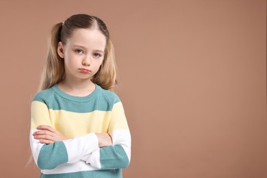 Photo of Portrait of sad girl with crossed arms on light brown background, space for text