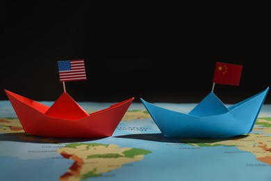 Photo of Paper boats with USA and China flags on world map against black background. Trade war concept