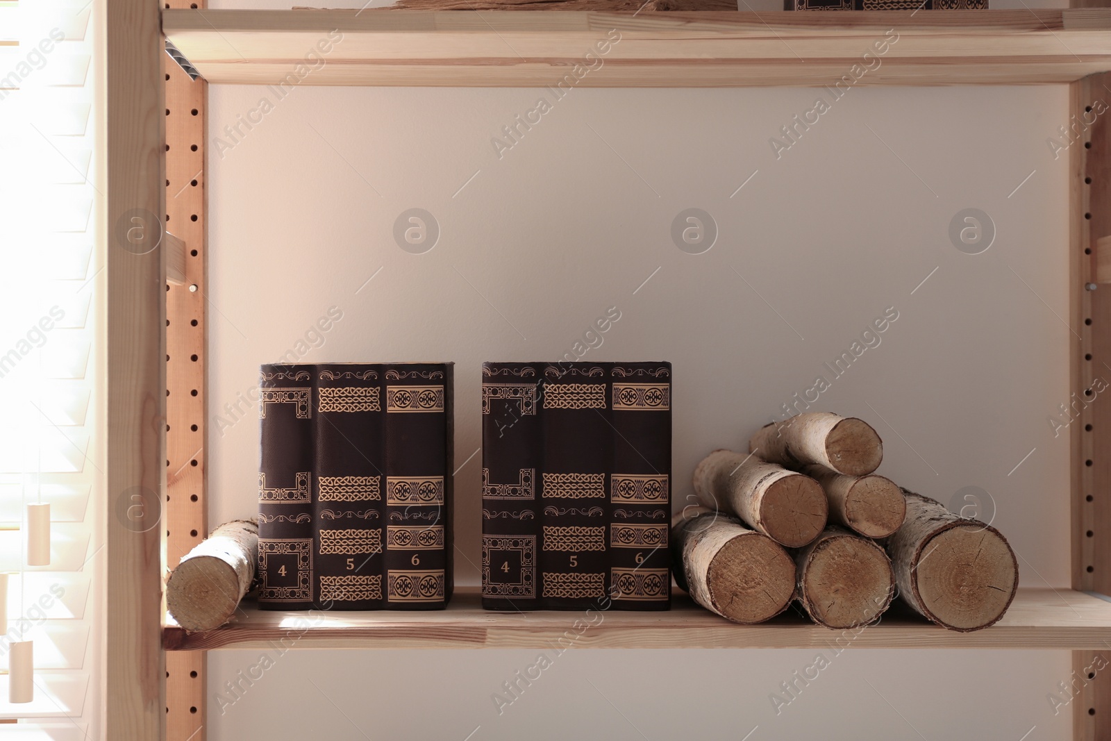 Photo of Shelving unit with stacked firewood and books near wall. Idea for interior design