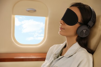 Photo of Young woman with sleep mask resting while listening to music in airplane during flight