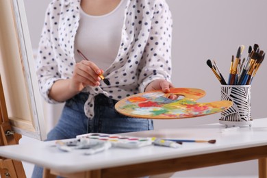 Photo of Woman artist drawing picture on canvas indoors, closeup
