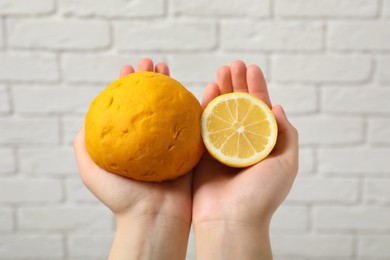 Photo of Woman holding dough painted with natural food coloring and lemon near white brick wall, closeup