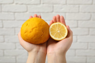 Woman holding dough painted with natural food coloring and lemon near white brick wall, closeup