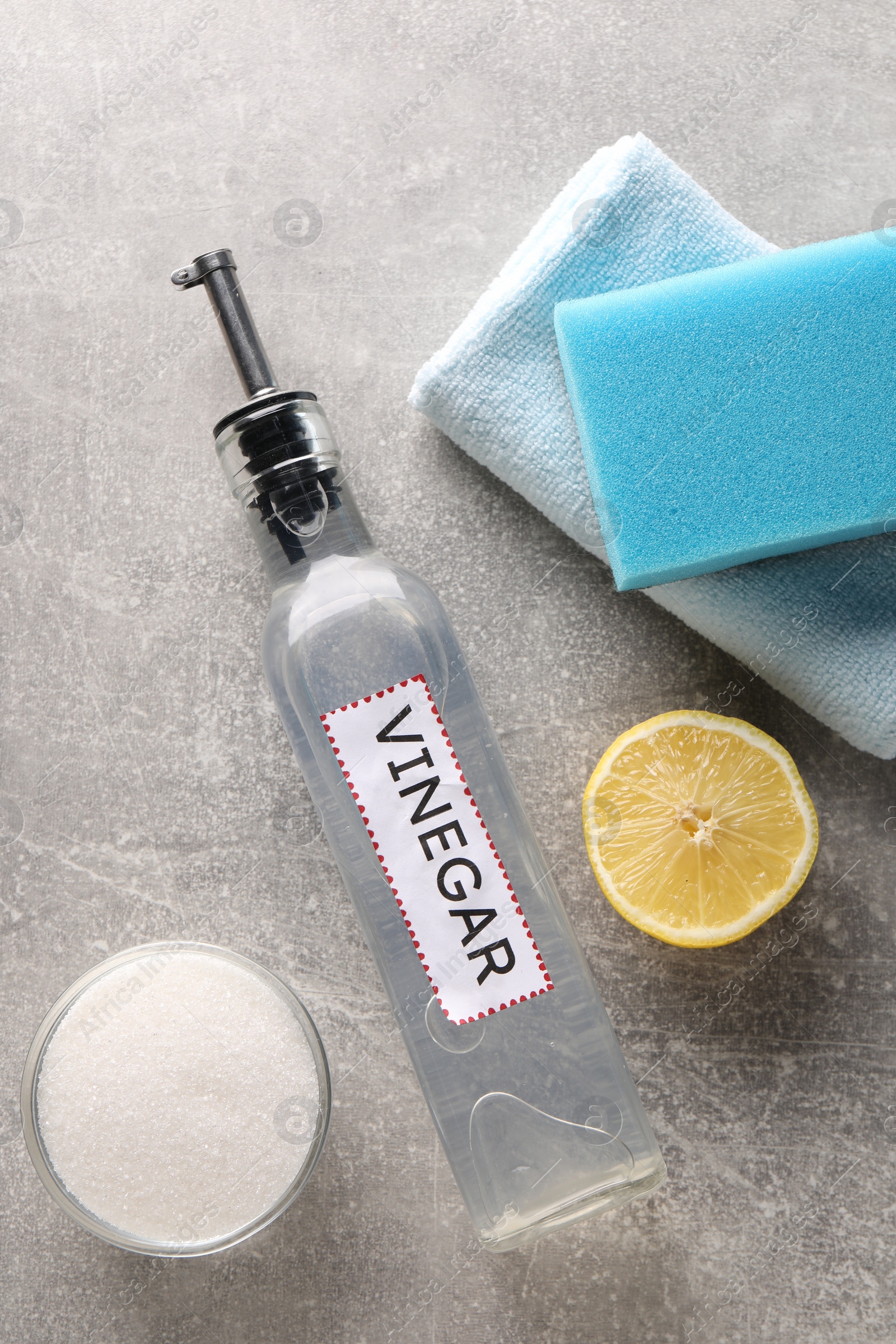 Photo of Natural cleaning products. Vinegar in bottle, baking soda, lemon, rag and sponge on grey textured table, flat lay