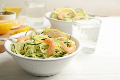 Photo of Delicious zucchini pasta with shrimps and lemon in bowl served on white wooden table