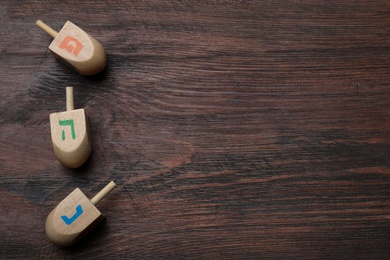 Photo of Hanukkah traditional dreidels with letters He, Pe and Nun on wooden table, flat lay. Space for text
