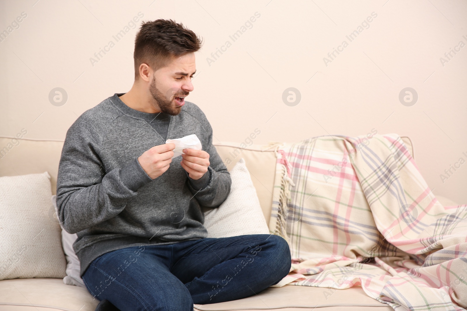 Photo of Sick young man sneezing at home. Influenza virus