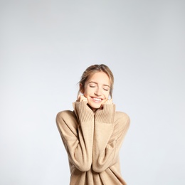 Beautiful young woman wearing knitted sweater on light grey background