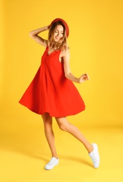 Photo of Beautiful young woman in red dress dancing on yellow background