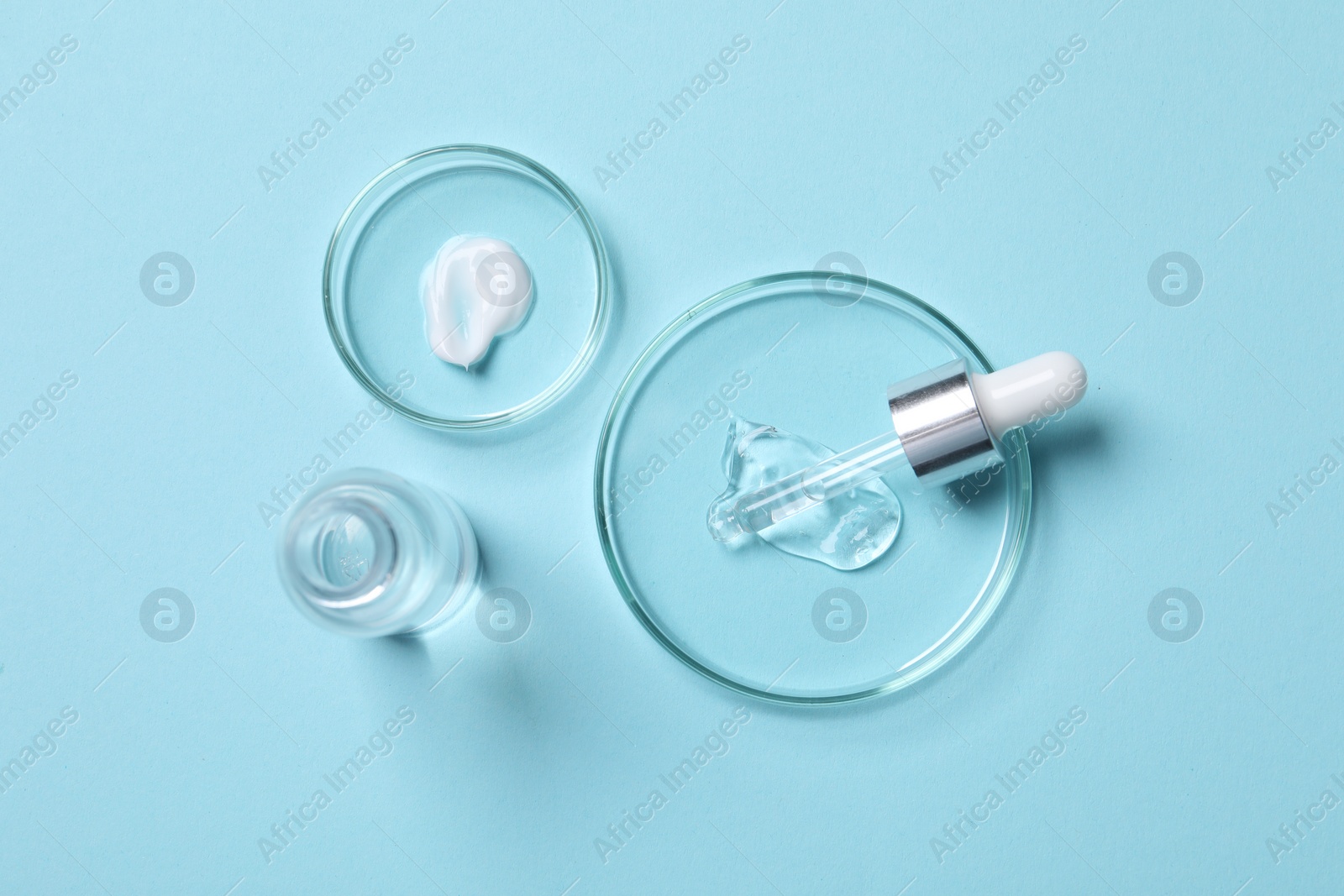 Photo of Petri dishes with samples of cosmetic serums, bottle and pipette on light blue background, flat lay