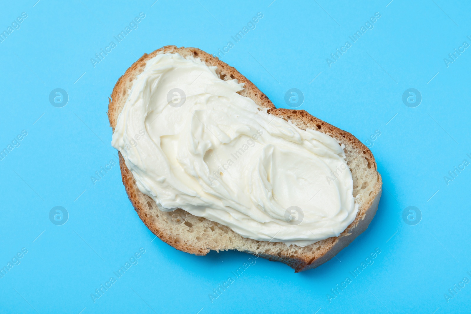 Photo of Slice of bread with tasty cream cheese on light blue background, top view