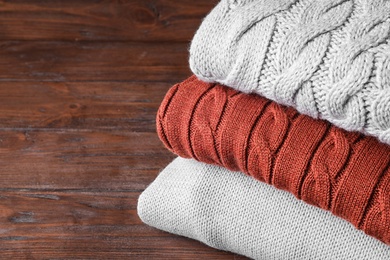 Stack of folded warm sweaters on wooden background, closeup