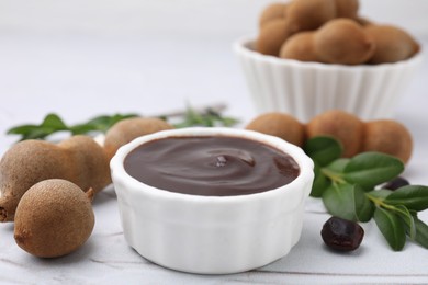 Photo of Bowl of tasty tamarind sauce and fresh pods on white textured table