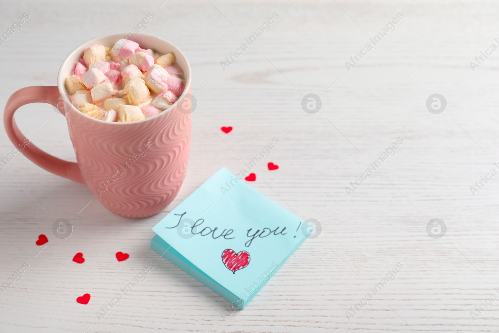 Photo of Note with phrase I Love You near pink cup of hot drink on white wooden table