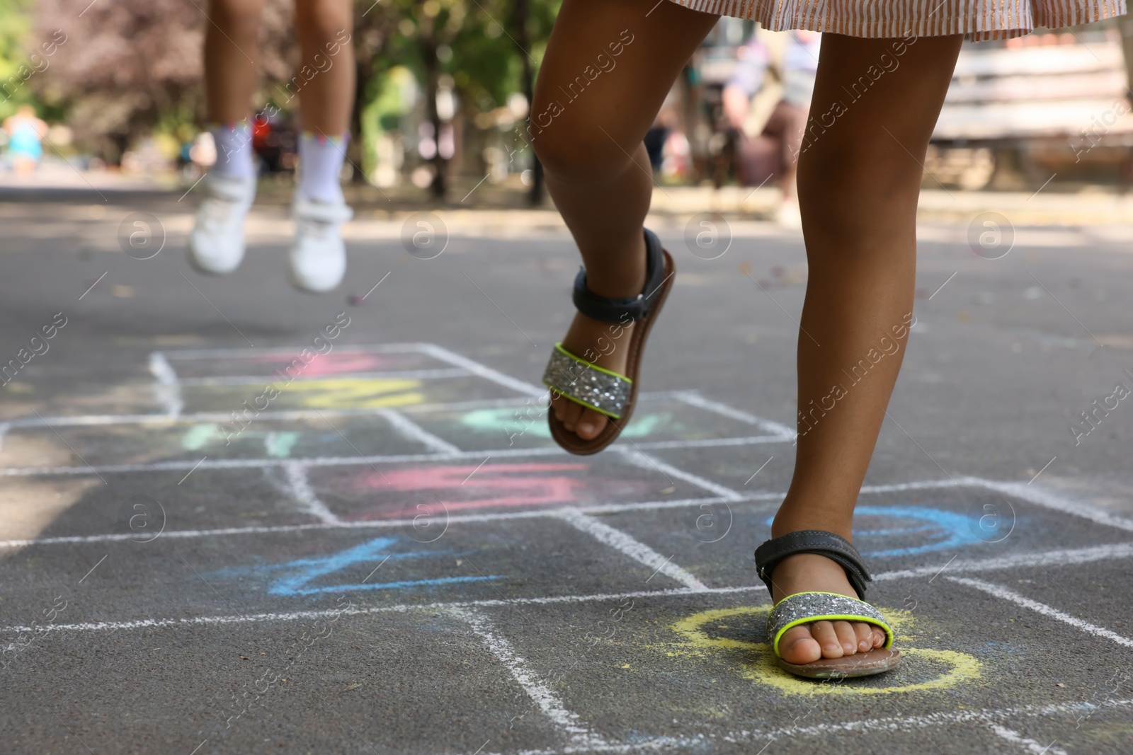 Photo of Little children playing hopscotch drawn with chalk on asphalt outdoors, closeup