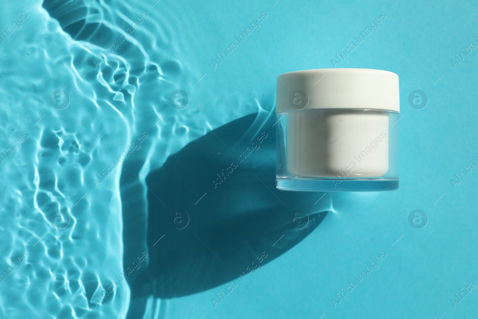 Photo of Jar with moisturizing cream in water on light blue background, top view. Space for text