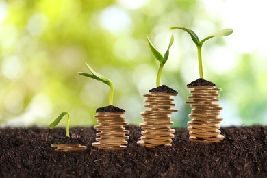 Image of Stacked coins and green seedlings on ground outdoors, bokeh effect. Investment concept