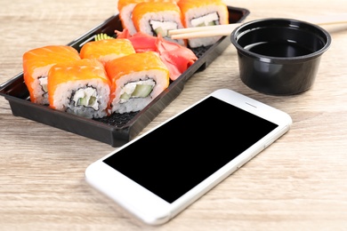 Photo of Smartphone with space for text and sushi rolls served on wooden table. Food delivery